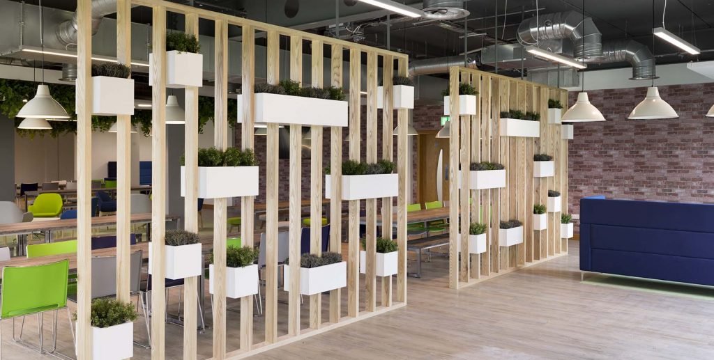 Artificial foliage planted in wooden troughs incorporated into a timber divider wall in a modern office breakout area