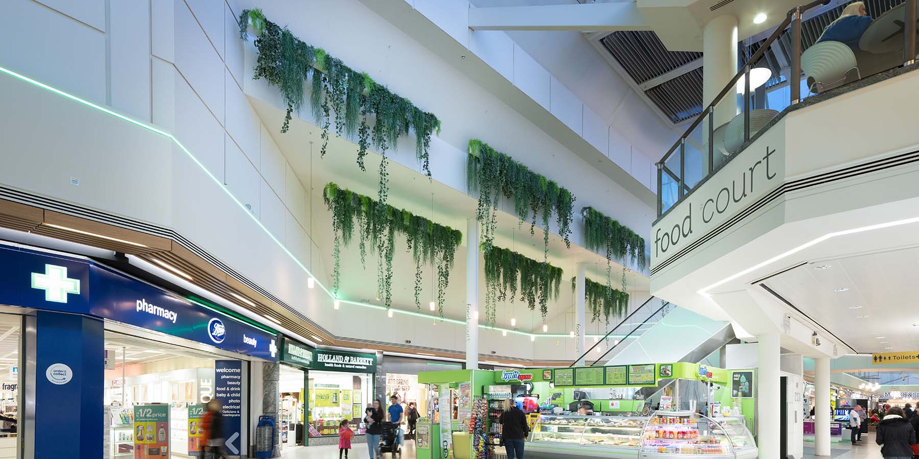 Trailing mixed artificial foliage cascades from bespoke hanging troughs high above retail units at Gyle Centre Edinburgh