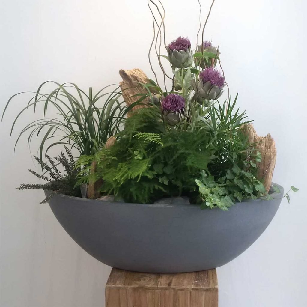 Artificial thistles, greenery and wooden accents in grey planter to dress a whisky distillery reception desk