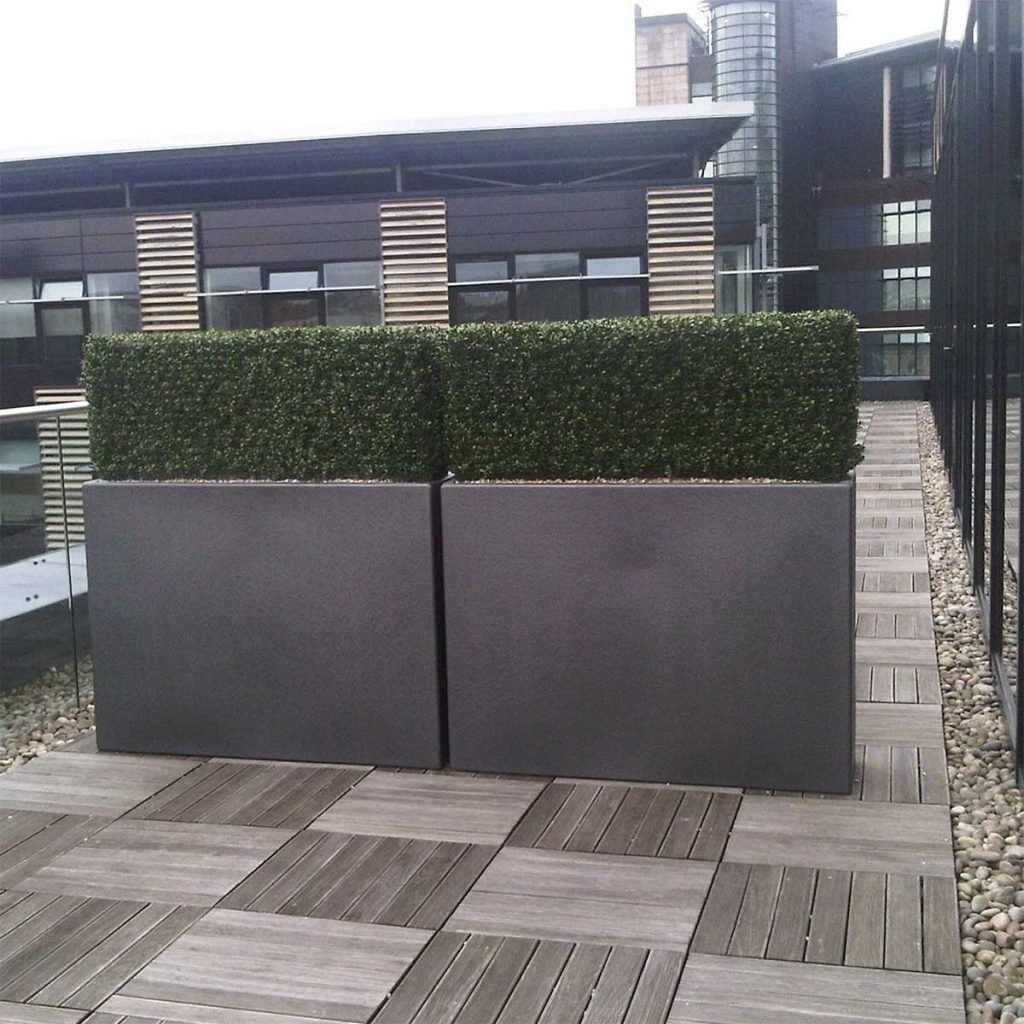 Tall slim grey planters with artificial hedging help separate and zone space on a city centre roof terrace