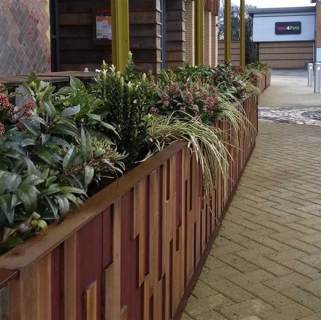 Exterior wooden planters filled with plants and greenery dividing outside dining space in a retail park