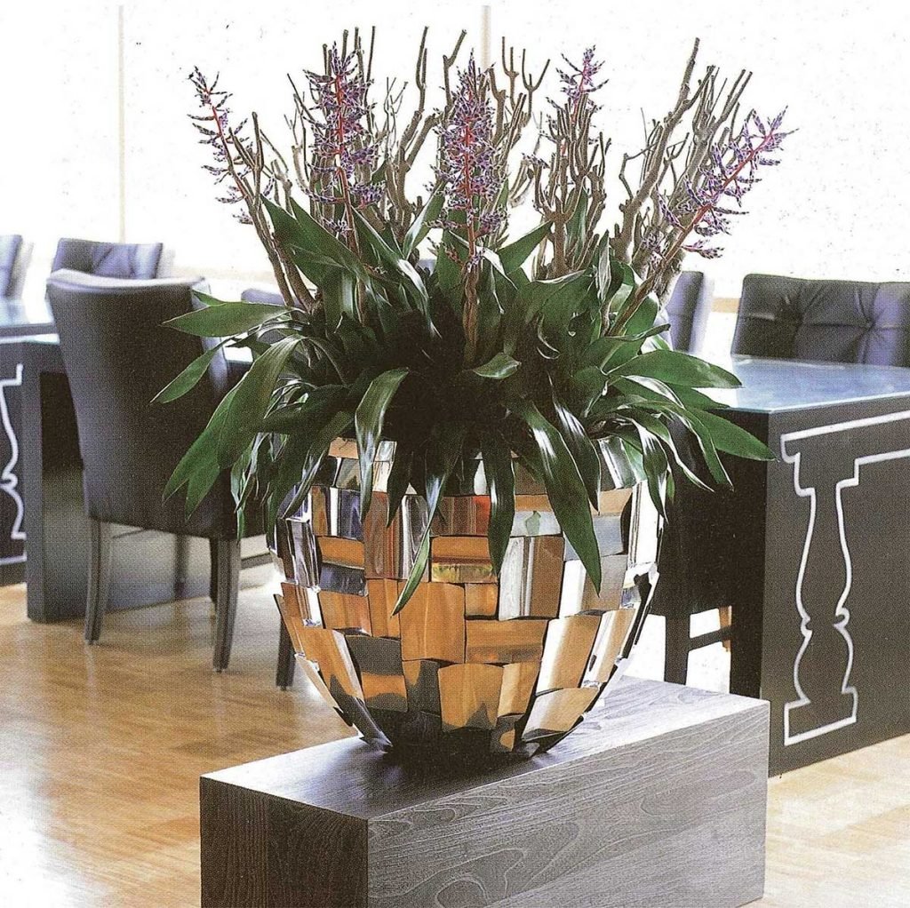 metallic finish pot on a grey wood effect plinth filled with green tones and textures in a restaurant setting