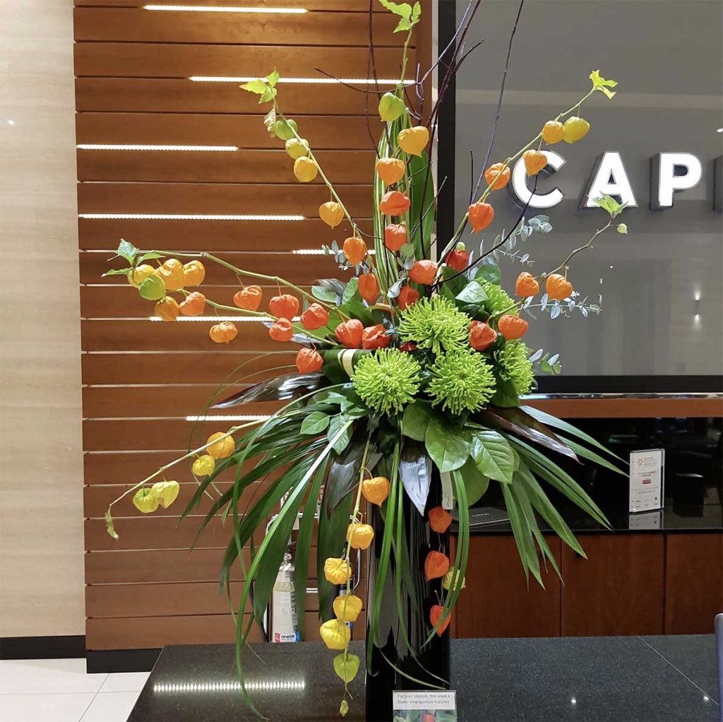 Tropical inspired flowers for a reception design in a tall gloss black vase in front of a modern wooden wall