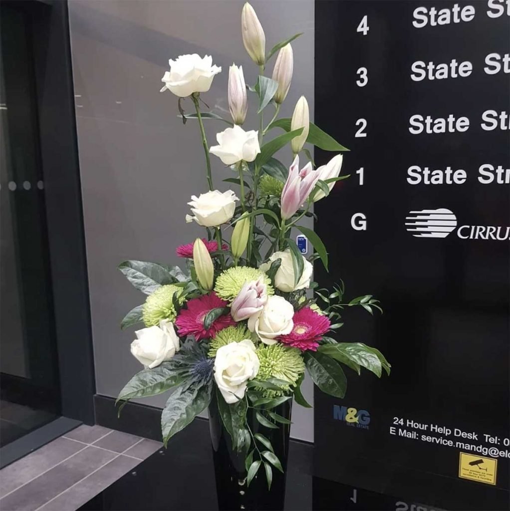 A tall floral reception arrangement filled with freshly cut flowers and foliage including white roses, lilies and gerbera