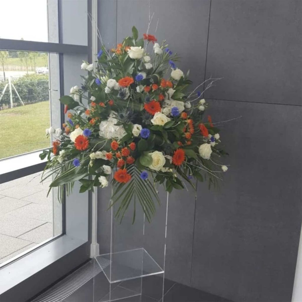 Fresh mixed flower pedestal arrangement with red, purple white and leafy foliage on a perspex stand