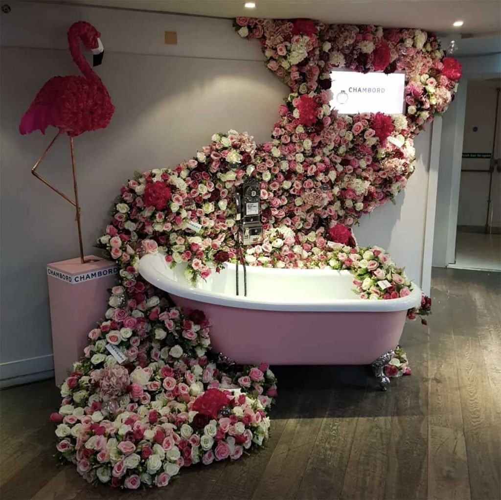 Vintage pink bathtub and phone surrounded by artificial roses and mixed greenery with a lightbox sign