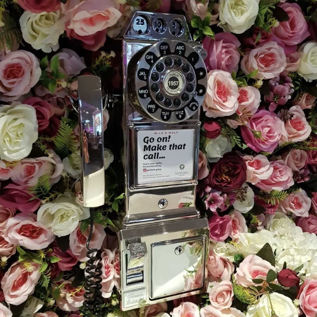 Vintage phone surrounded by artificial pink and cream roses with greenery, part of a cocktail bar installation