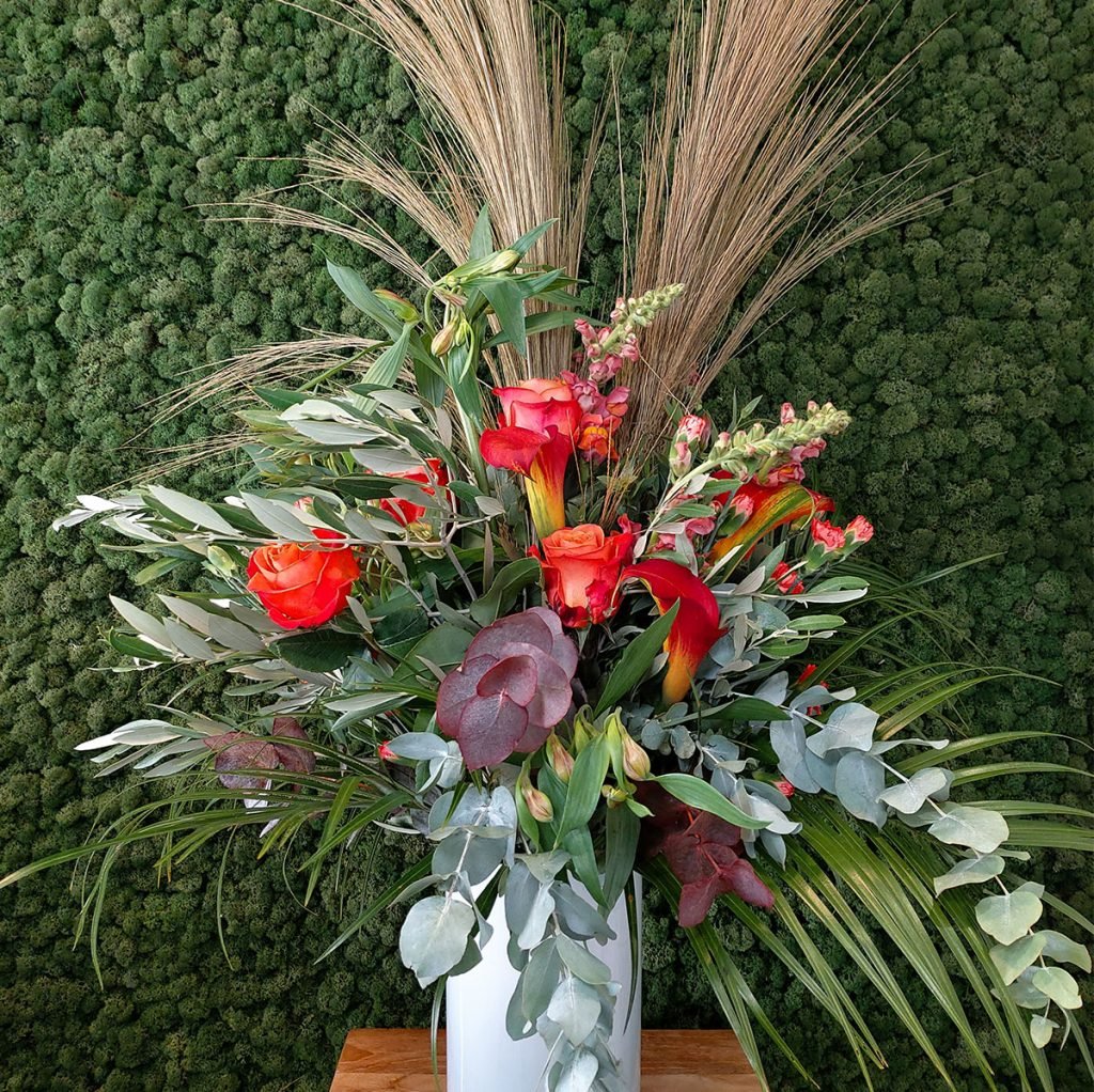 white vase with corporate display featuring red cala lilies, snapdragons, eucalyptus and dried grain grass
