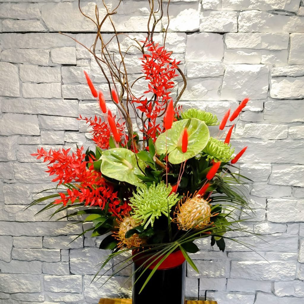 corporate flower display in black vase with bold flowers e.g. green anthuriums, chrysanthemums and dried red bunny tails and ruscus