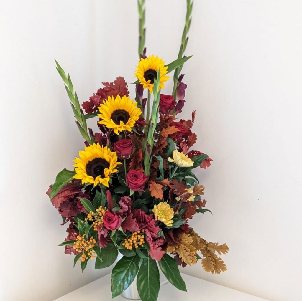 gorgeous autumn themed corporate flower display featuring sunflowers, gladiolii, roses and autumn leaves