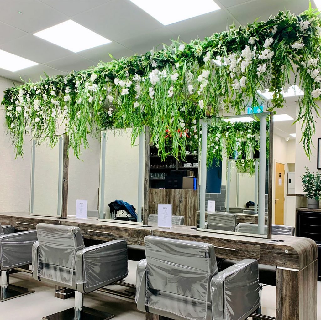 Gorgeous hairdresser's interior looks extra special with these hanging plants and white blossom trails, creating a magical vibe that pairs perfectly with the sleek, modern furniture