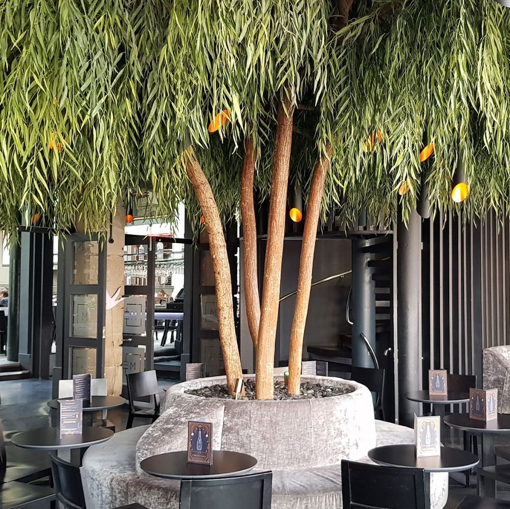 tall bespoke built artificial weeping willow tree with a round seating bench built around it inside a restaurant