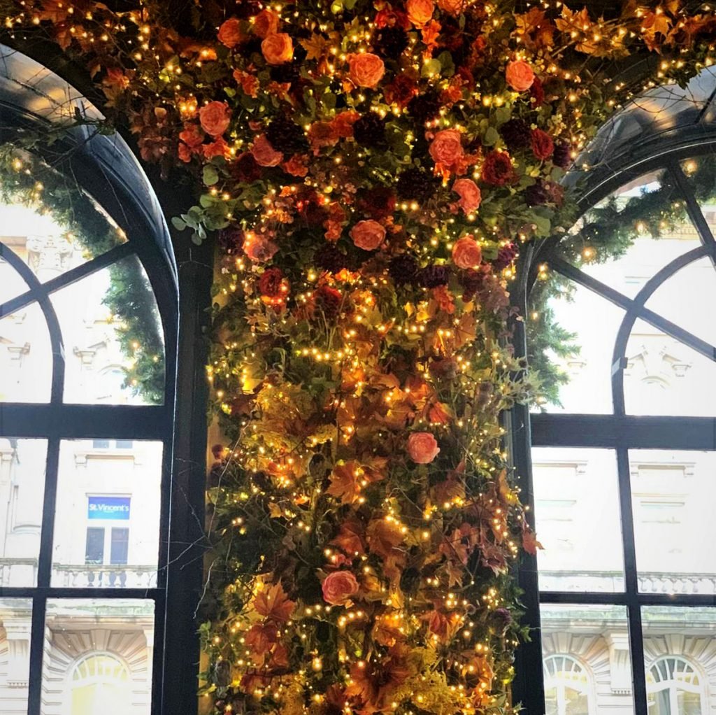 stunning floral display built between two arched windows and creeping over to create a magical atmosphere within the restaurant - featuring autumn coloured flowers, pink accent, twisted vines and fairy lights