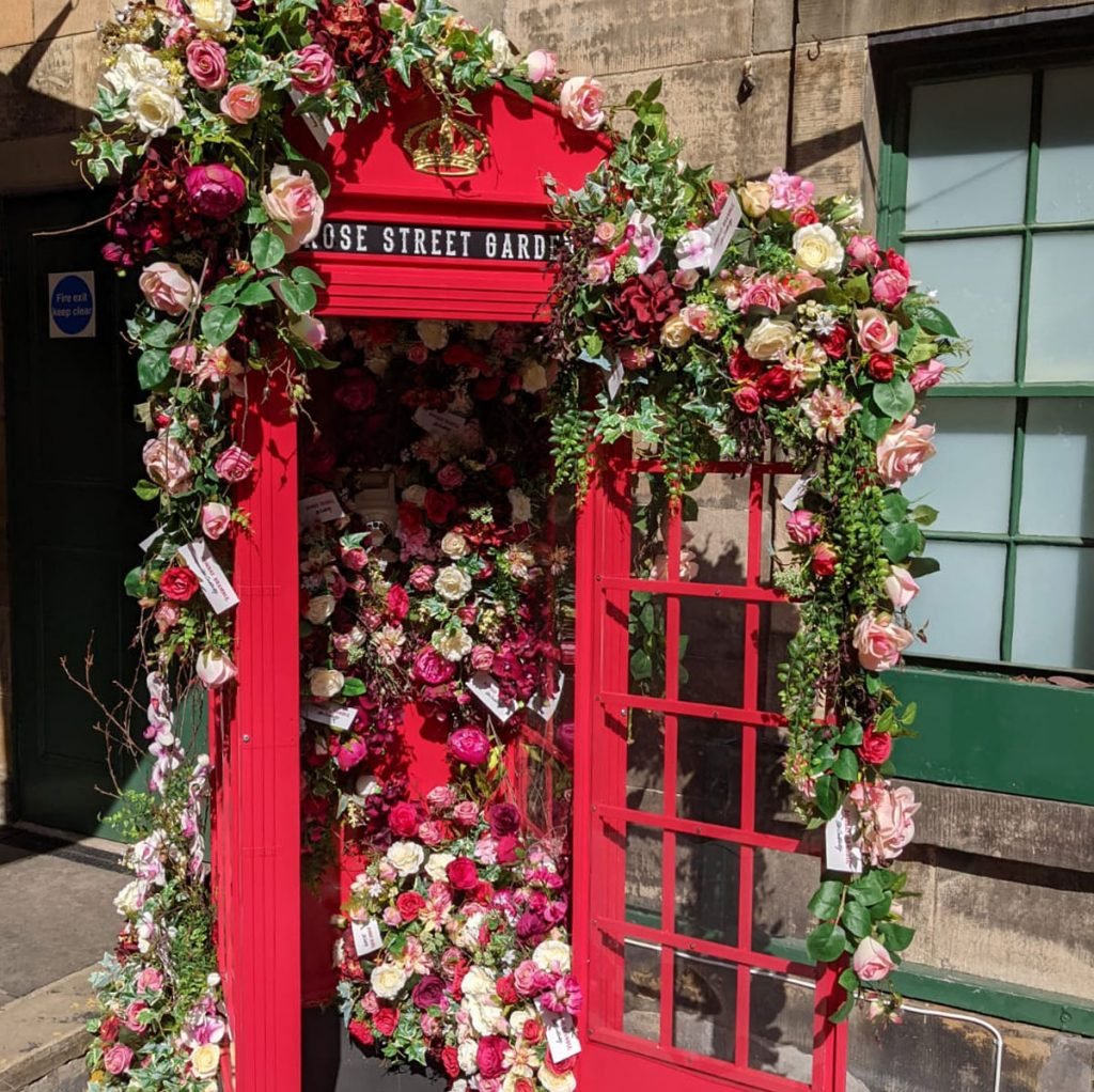 bespoke painted phonebox decorated lavishly with artificial flower displays, artistically draped over the door and cascading from inside to create the perfect selfie spot at rose street gardens in edinburgh