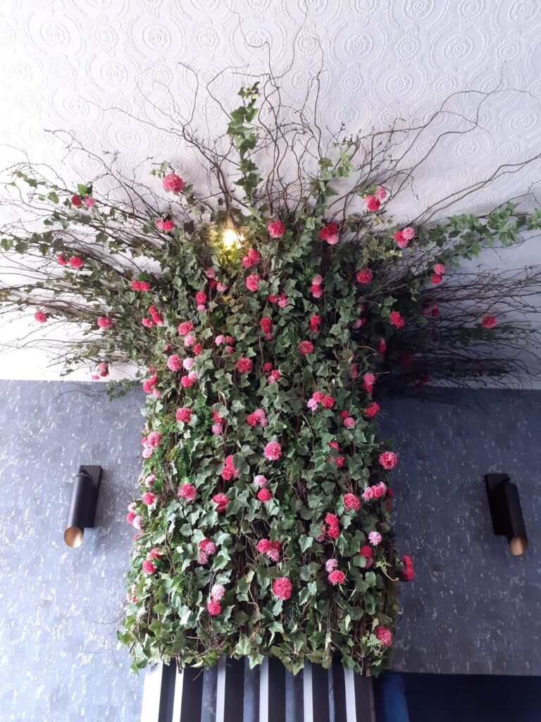 Vibrant artificial pink flowers and branched ivy make up this stunning floral display that spans from a pillar to the ceiling