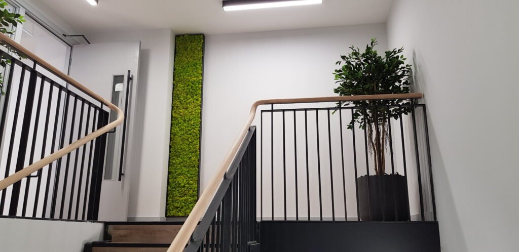 A vibrant spring green moss panel and artificial tree improve this stairwell.