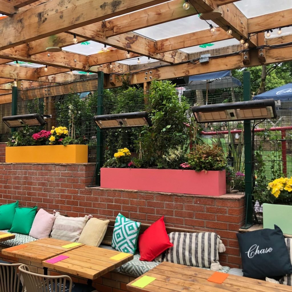 Pink and orange troughs filled with lush planting and flowers sit atop a wall in Brel Glasgow's outdoor dining area