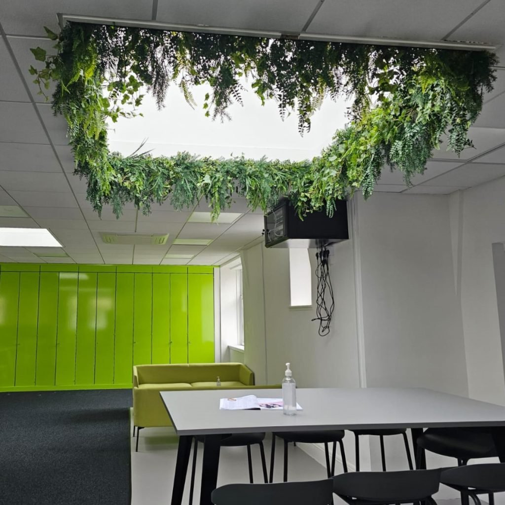 a ceiling lightwell above desks is lined with artificial trailing strip planting