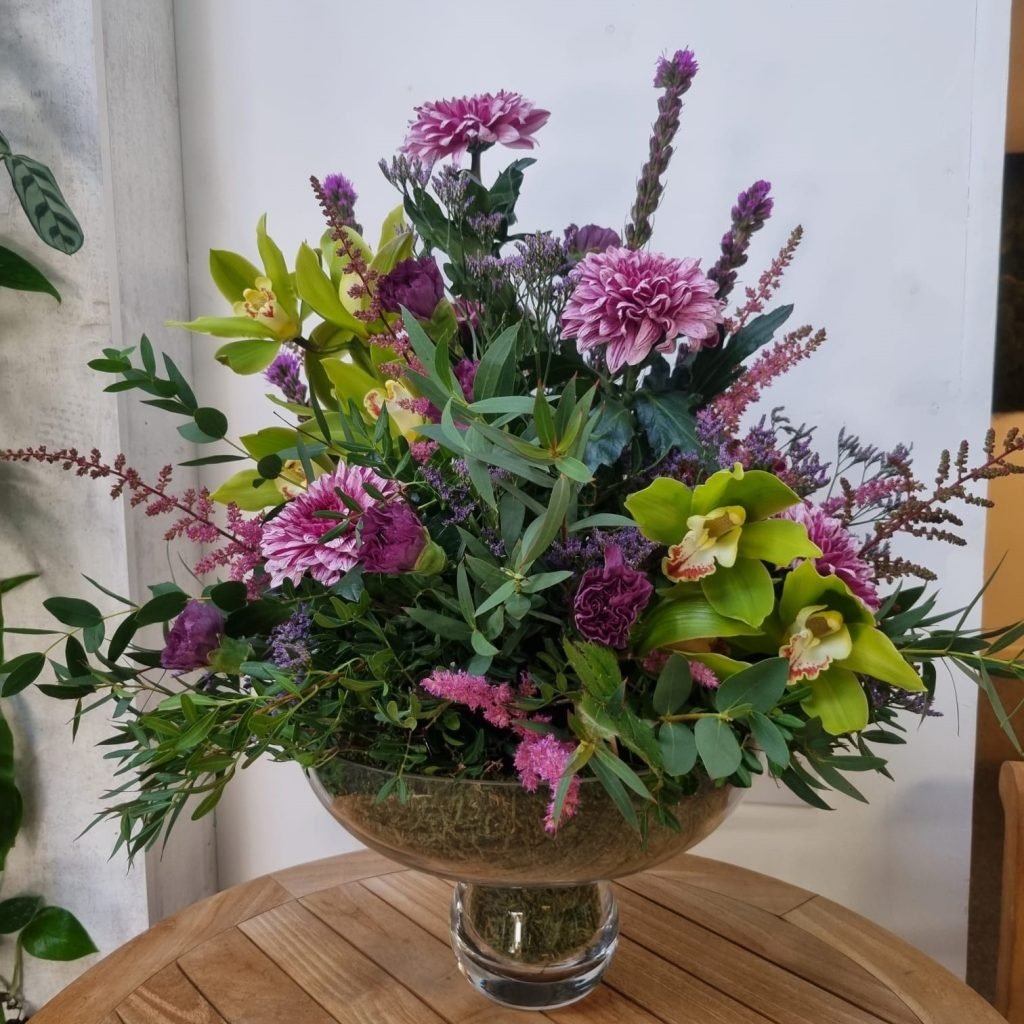 Beautiful purple and pink flowers sit in a decorative bowl vase for an office reception desk